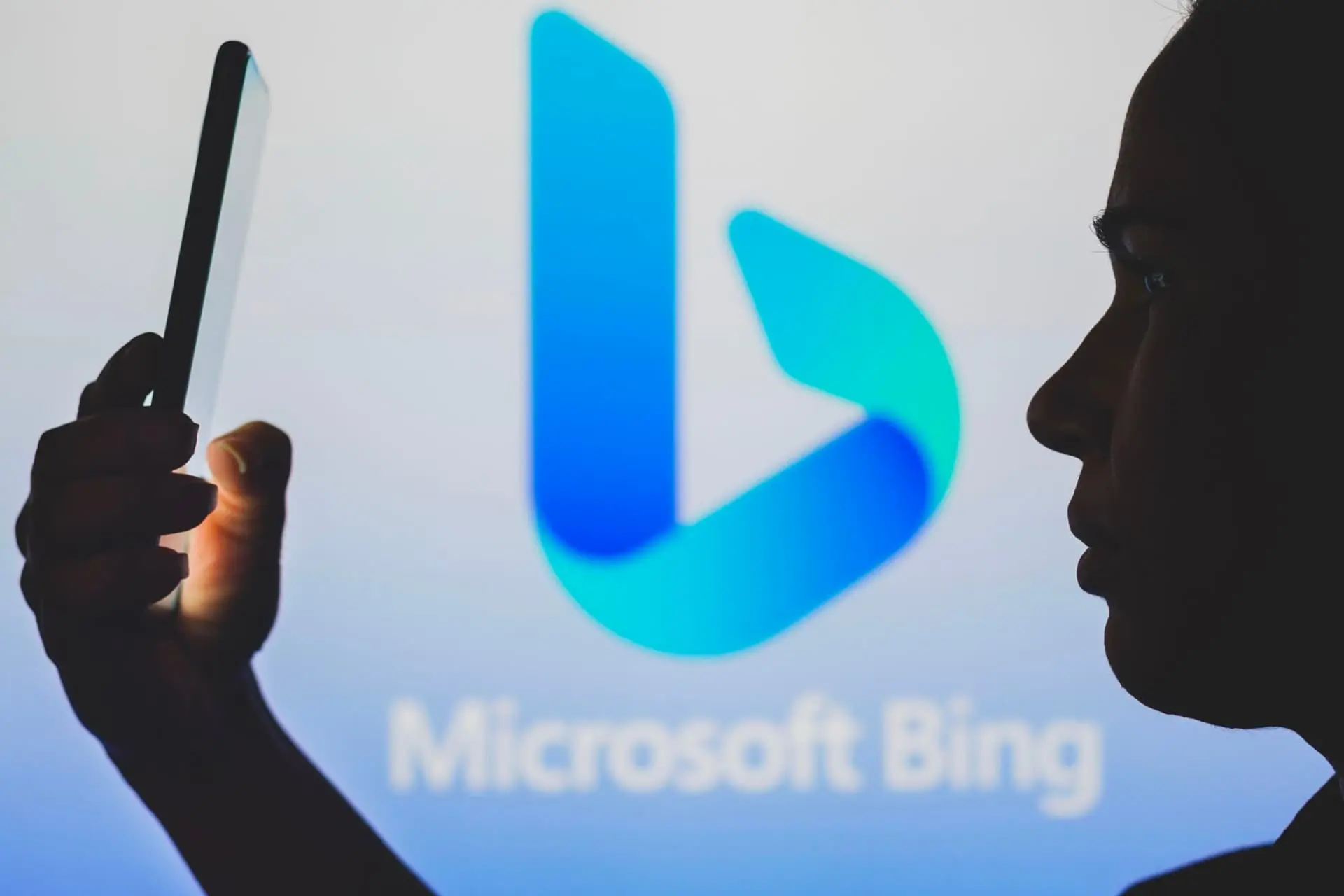 A woman with a mobile phone in front of the Microsoft Bing logo / Microsoft Bing